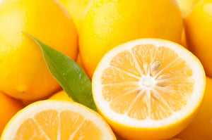 Freshly cut Meyer lemon halves showing juicy golden flesh alongside whole ripe lemons and a green leaf.