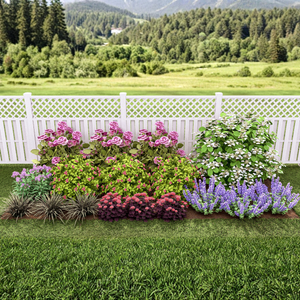 A beautifully arranged garden flower bed planted along a white lattice-top fence, featuring blooming pink roses, large white hydrangeas, and purple salvia set against a scenic mountain landscape background.